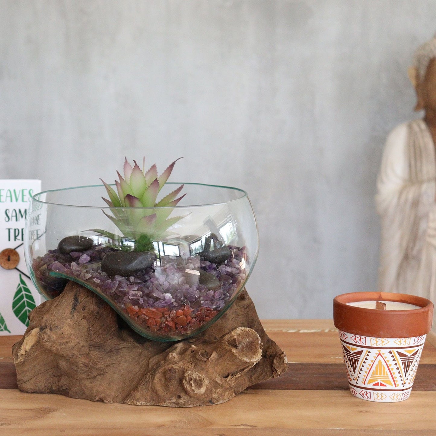 Glass terrarium with succulent on a wooden base next to a patterned candle in a pot.