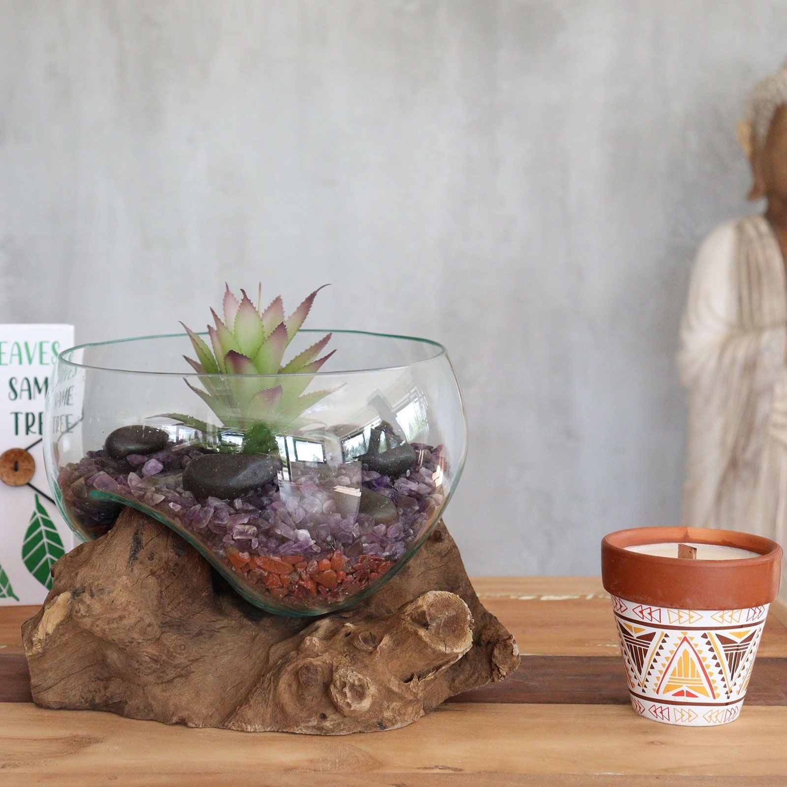 Glass terrarium with succulent on a wooden base next to a patterned candle in a pot.