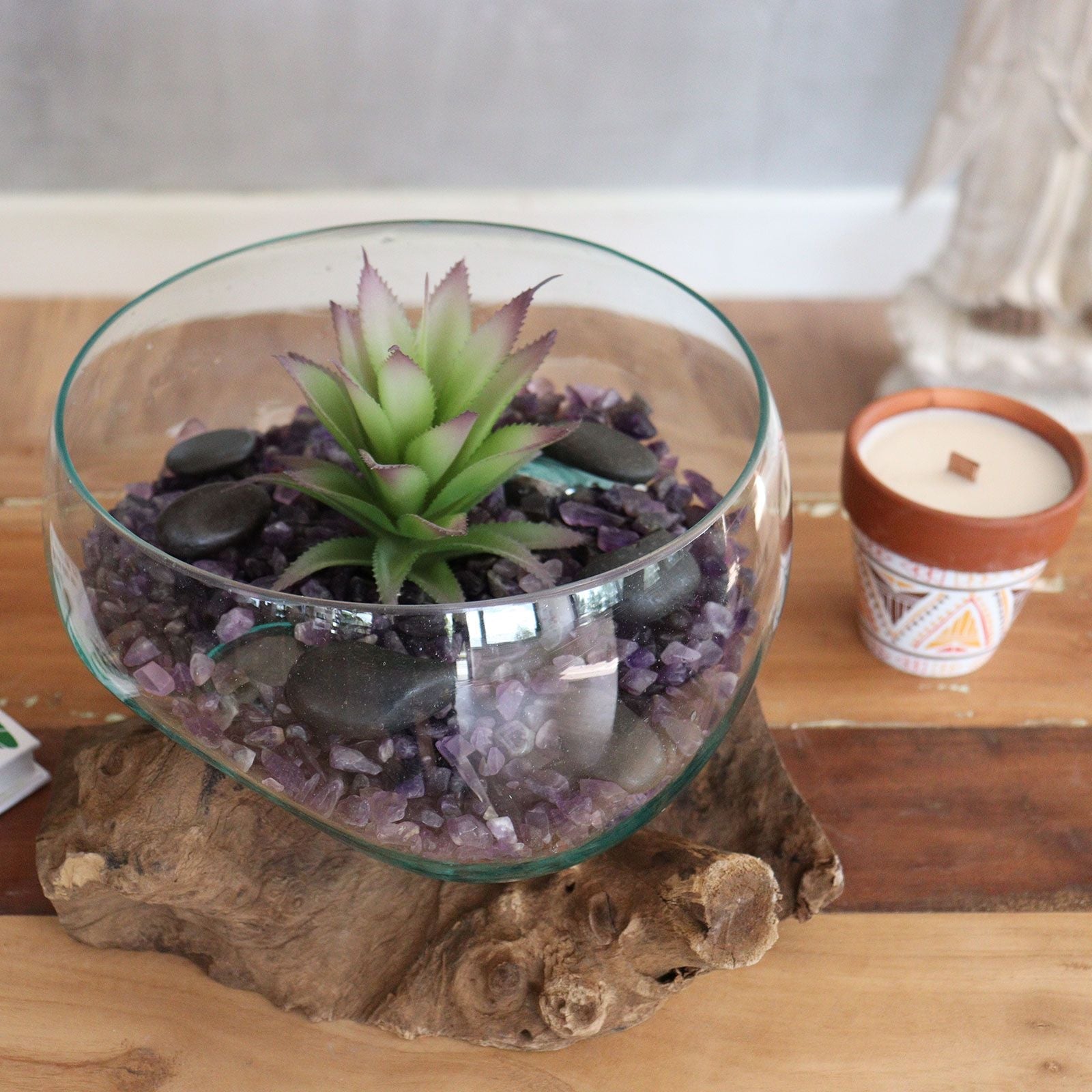 Glass terrarium with succulent on a wooden base next to a patterned candle in a pot.