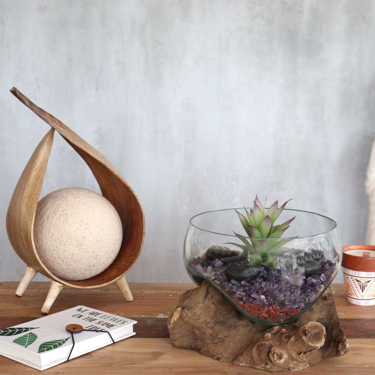 Glass terrarium with succulent on a wooden base next to a patterned candle in a pot.