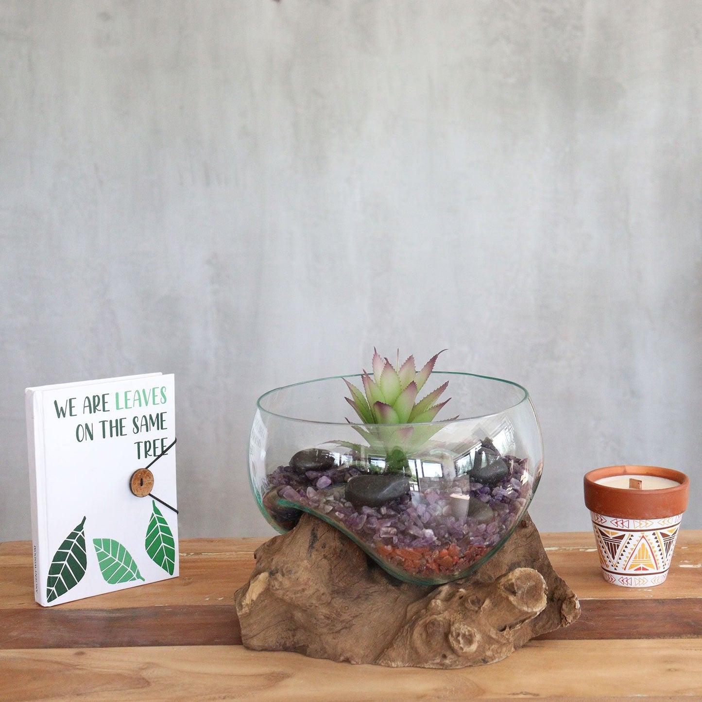 Glass terrarium with succulent on a wooden base next to a patterned candle in a pot.